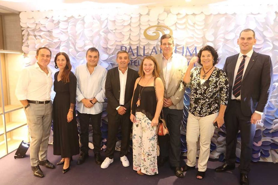 Ocho personas posan sonrientes frente a una pared blanca texturizada con el logo y el texto "PALLADIUM HOTELS & RESORTS".