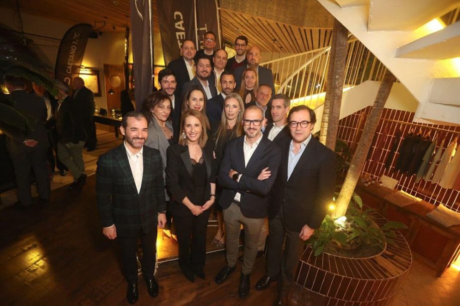 Un grupo de unas 20 personas posa sonriente en un interior moderno con escalera blanca y una bandera oscura al fondo con el texto "CVEC T".