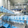Cajas de cartón azules claras avanzan por múltiples cintas transportadoras en una moderna planta industrial de alimentos, entre maquinaria de acero inoxidable y con personal.